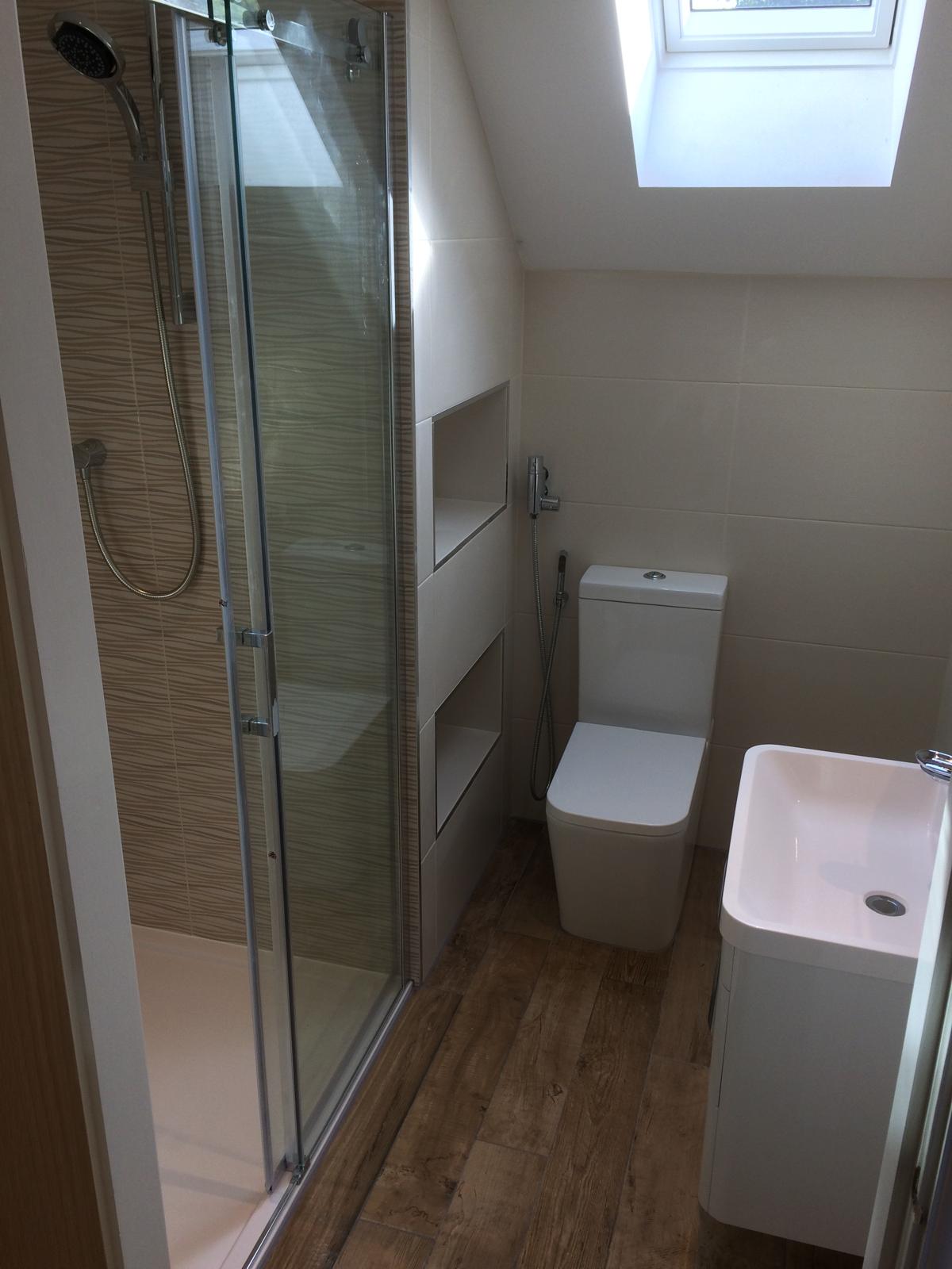 Compact loft en-suite with sliding-door shower enclosure, twin recessed wall niches, Velux rooflight and engineered wood-effect flooring.