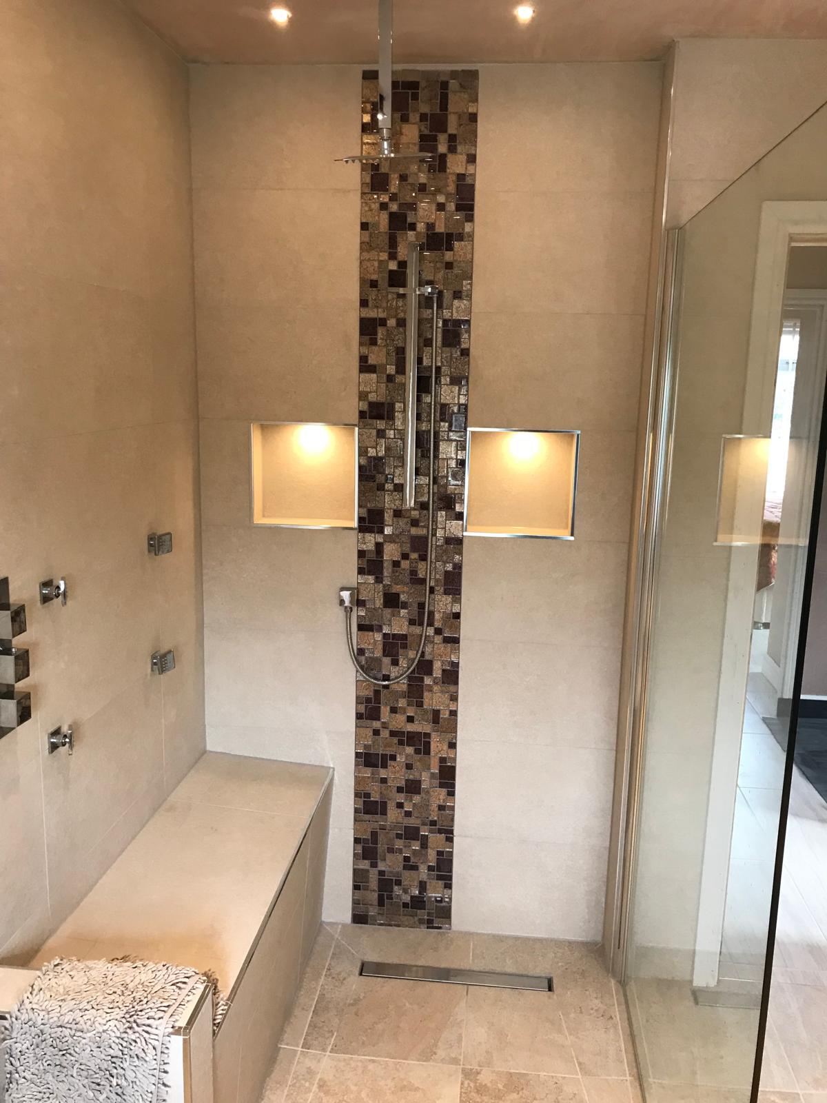 Luxury walk-in shower with full-height mosaic feature strip, twin recessed niches with downlights, tiled bench seat and linear floor drain.