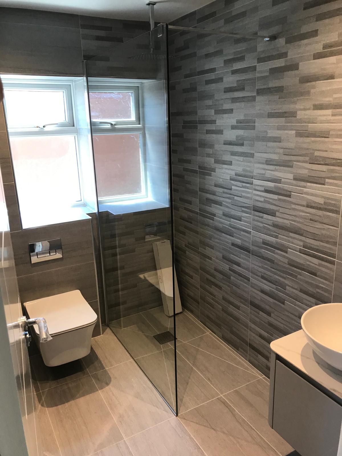 Fully tanked wet room with graphite brick-effect feature wall, wall-hung WC, frameless glass screen and tiled-in linear drain.