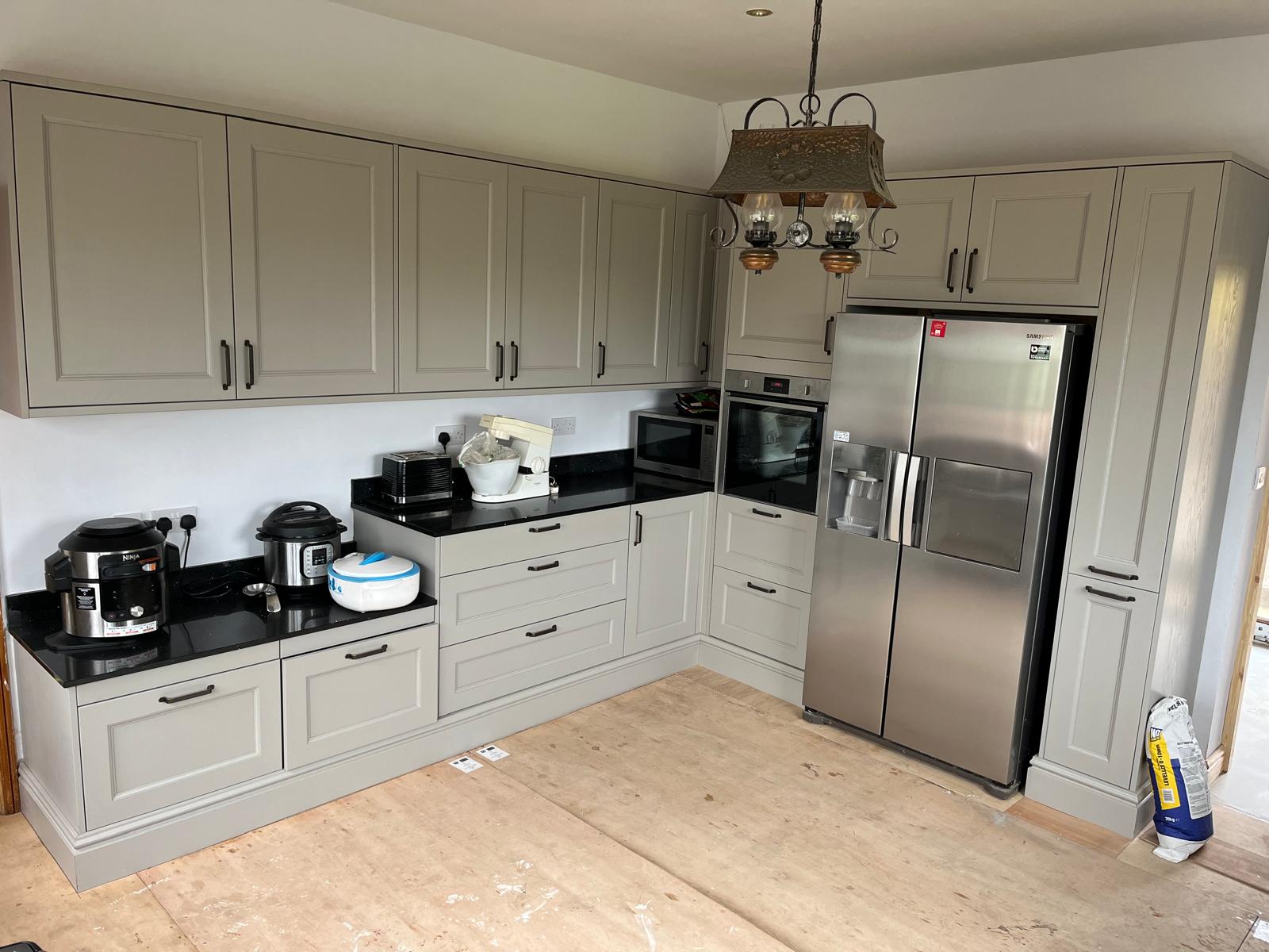 Classic stone-coloured shaker kitchen with deep black quartz worktops, double oven, microwave tower and American-style fridge freezer.