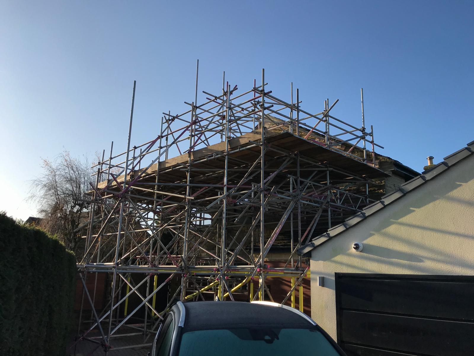 Scheme-specific scaffold built to ridge height with raking shores and timber spreader plates to physically restrain a bulging gable wall under truss thrust.
