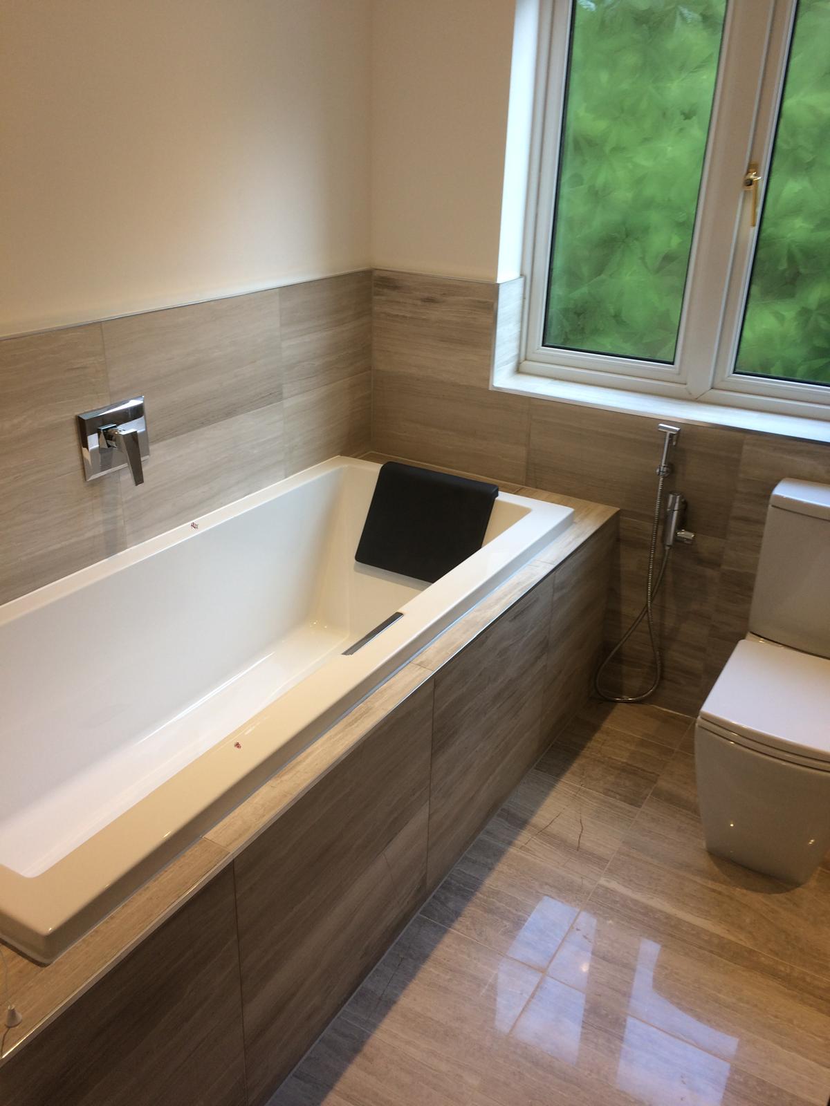 Full family bathroom refit with panelled bath, wood-effect porcelain tiling, concealed cistern WC and brushed chrome fittings.