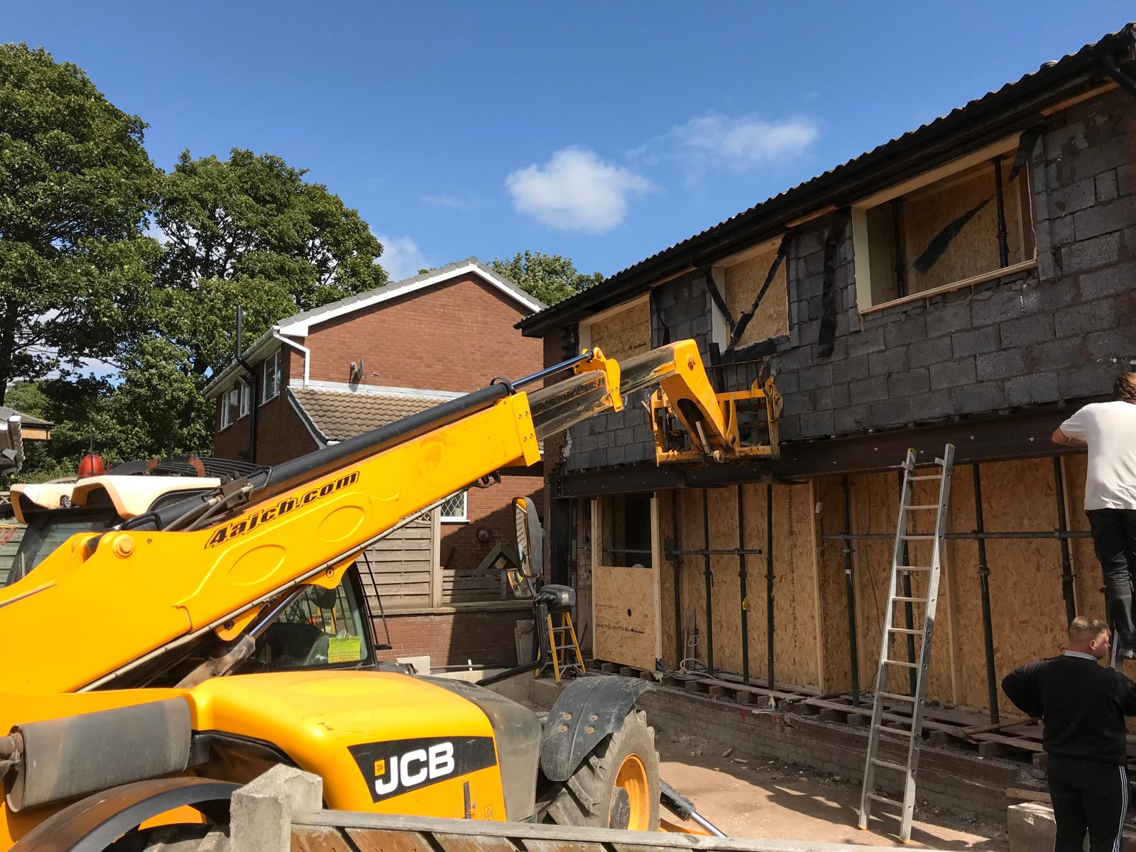 JCB telehandler lifting materials to the upper lift as the blockwork shell of a two-storey side extension takes shape, with new window openings formed and propped.