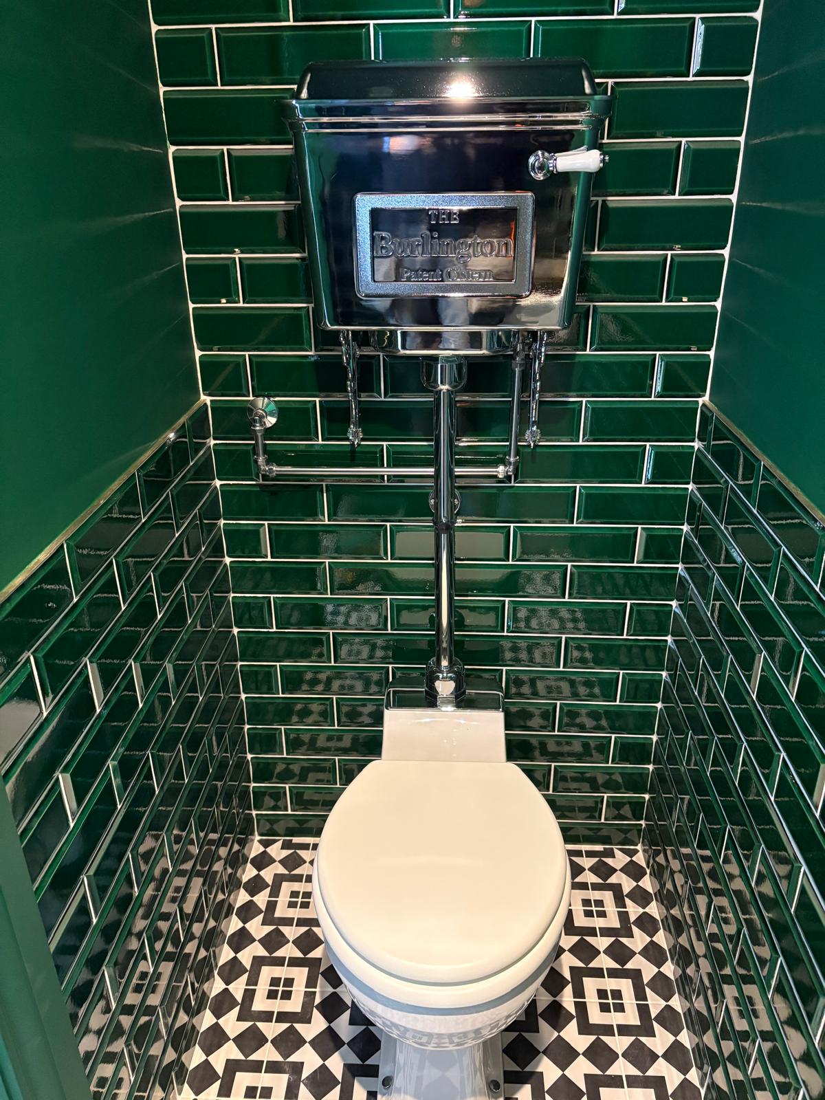 Close-up of a fully tiled emerald metro cloakroom featuring a polished chrome Burlington cistern, exposed chrome pipework and monochrome patterned floor tiles.