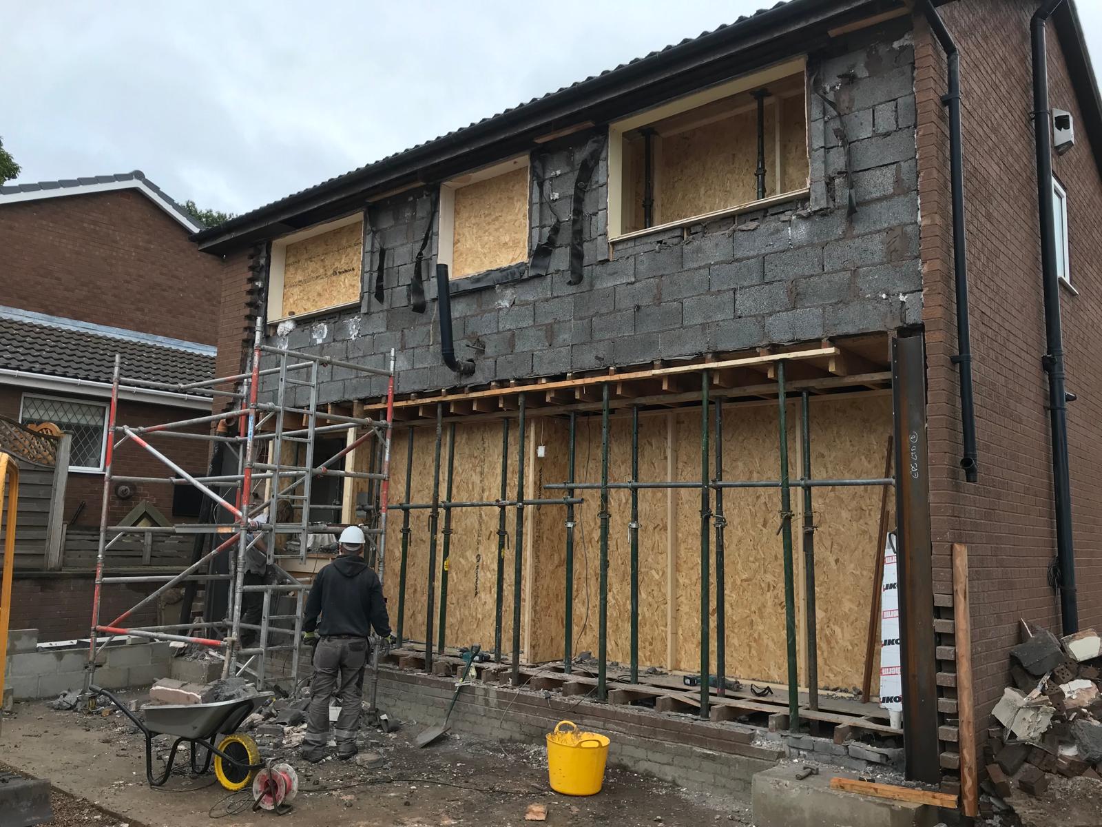 Structural steel beams and goalpost frame installed to support the upper storey, with adjustable Acrow props and OSB sheathing holding the ground floor opening during the build.