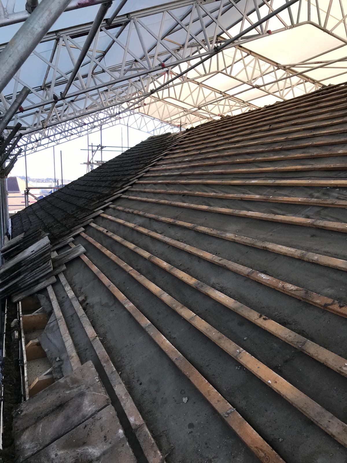 Tiles, battens and membrane stripped safely under a full encapsulating temporary roof — allowing structural works to continue regardless of weather.