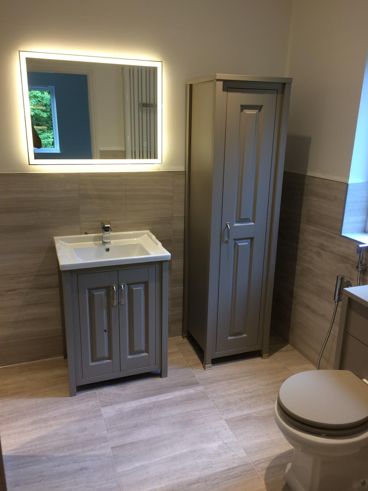 Classic shaker-style bathroom with grey vanity unit, matching tallboy, back-lit LED mirror and wood-effect feature tiling.