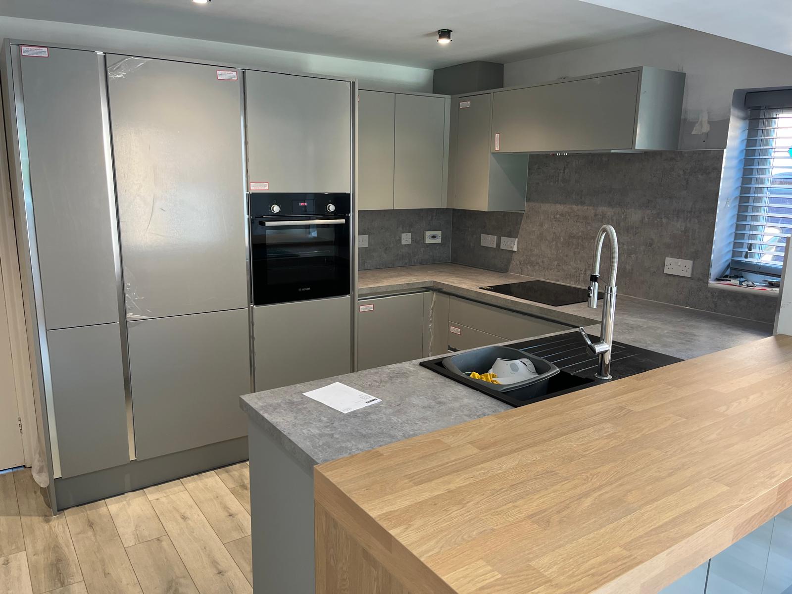 Compact U-shape handleless kitchen in sage with stone-effect worktops and matching upstand, oak peninsula breakfast bar and integrated Bosch appliances.