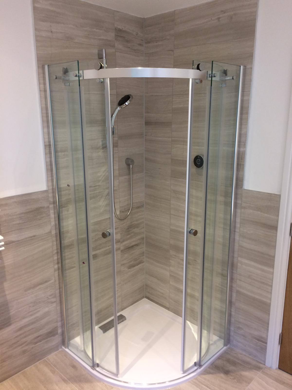 Curved quadrant shower enclosure with sliding doors, digital smart shower and travertine-effect porcelain tiling.