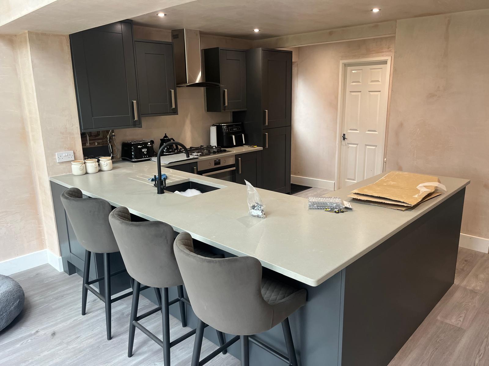 Charcoal shaker kitchen with stone-effect quartz peninsula and breakfast bar, chimney extractor and freshly skimmed walls ready for decoration.