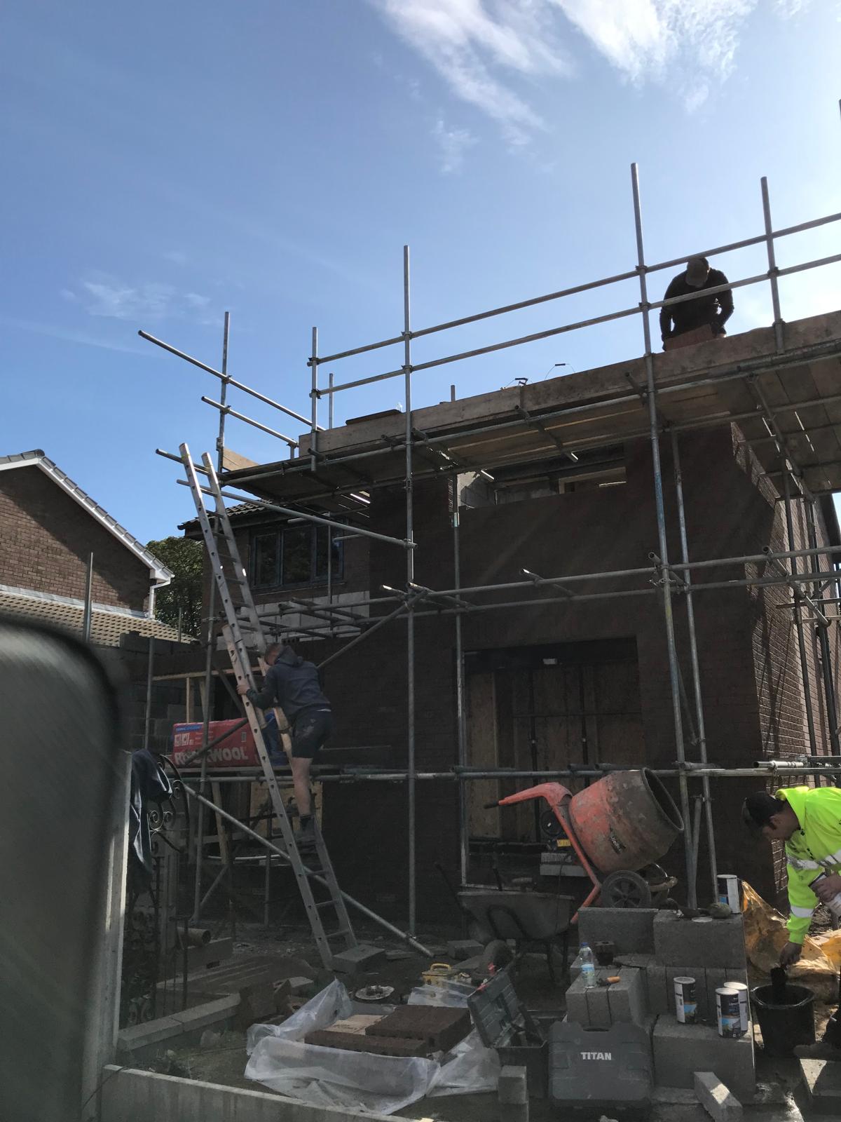 Second lift of brickwork progressing up to roof level on the two-storey extension, with scaffold in place for the next course and steel lintels set above openings.