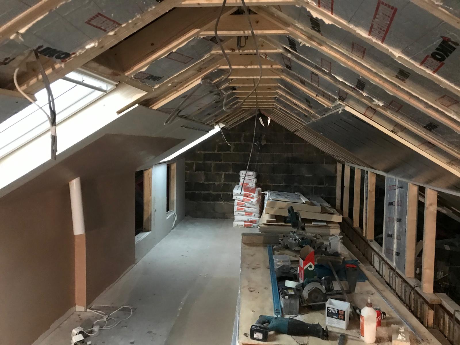 Foil-backed insulation board and plasterboard fixed between rafters with skylight openings framed in — thermal performance and airtightness addressed throughout.
