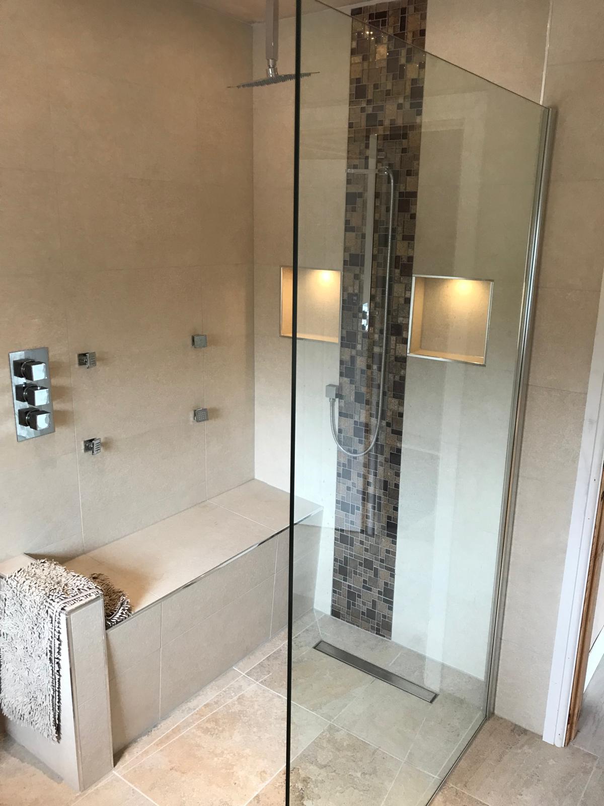 Frameless glass walk-in shower with ceiling rainfall head, body jets, mosaic feature strip and a built-in tiled bench seat.