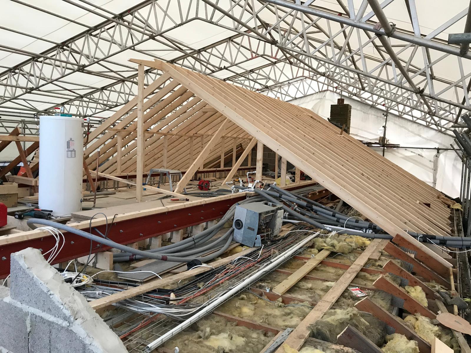 New structural steels craned in to carry the replacement roof, followed by engineered trusses lifted into position with proper restraint back to the masonry.
